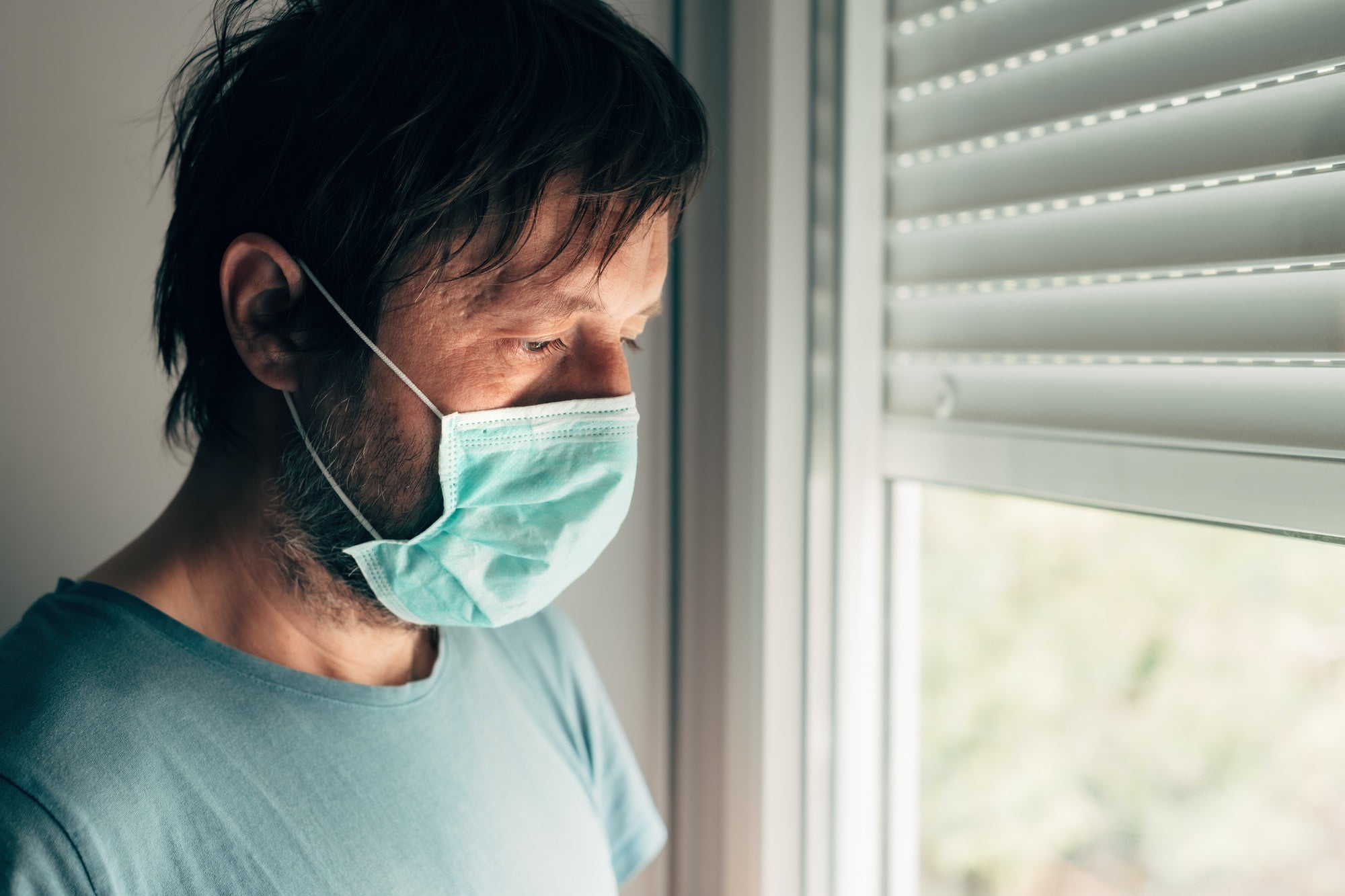 Depressed man with protective mask in self-isolation quarantine during virus outbreak pandemic