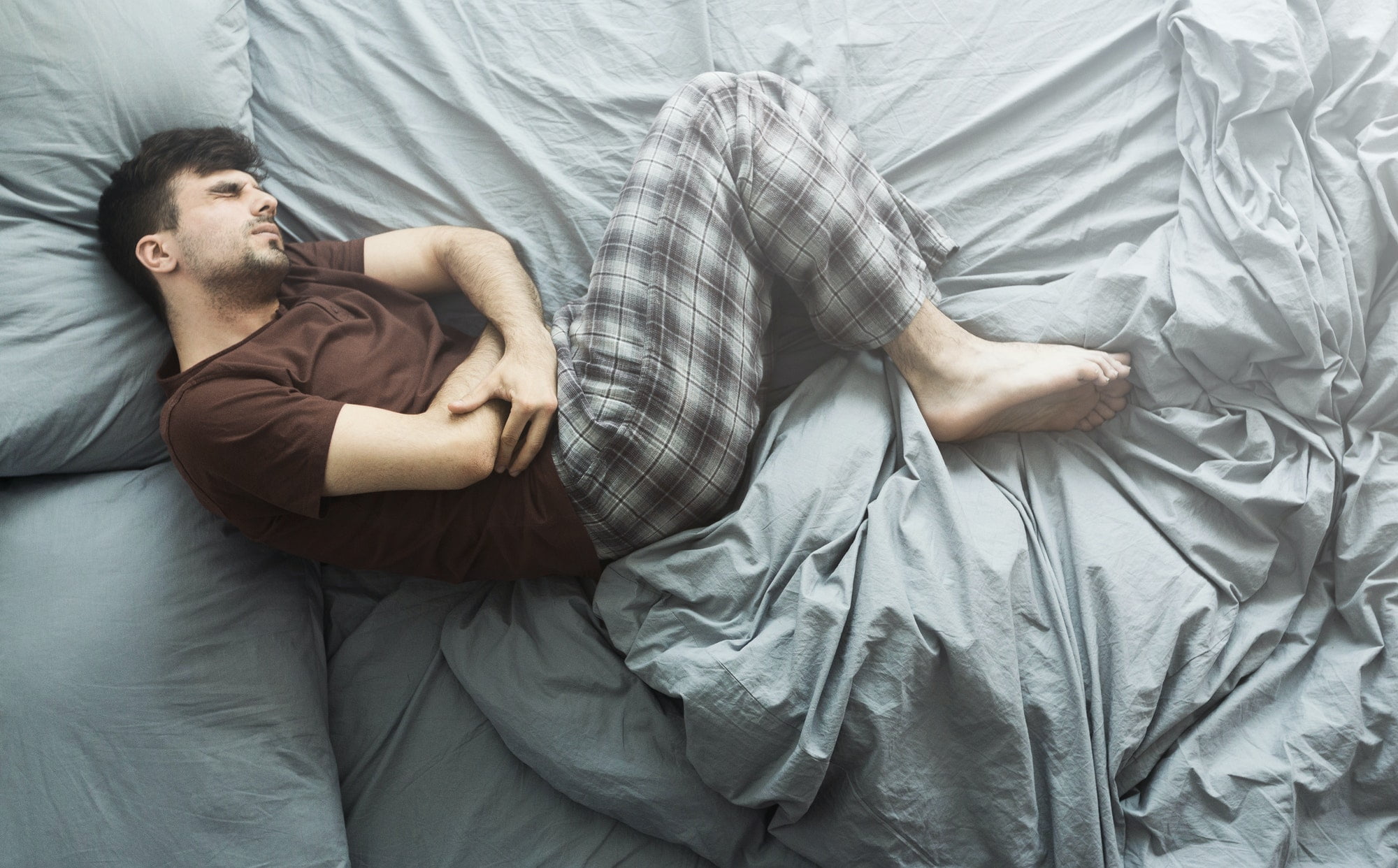 Man lying in bed having abdominal pain, top view