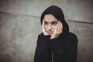 Anxious teenage girl in black hooded jacket standing with hand on face