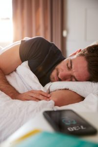 Man Asleep In Bed With Mobile Phone On Bedside Table