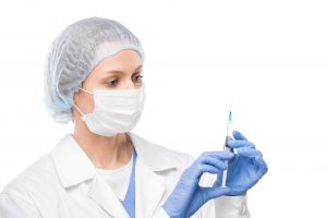 Nurse in protective mask, gloves and whitecoat holding syringe with vaccine