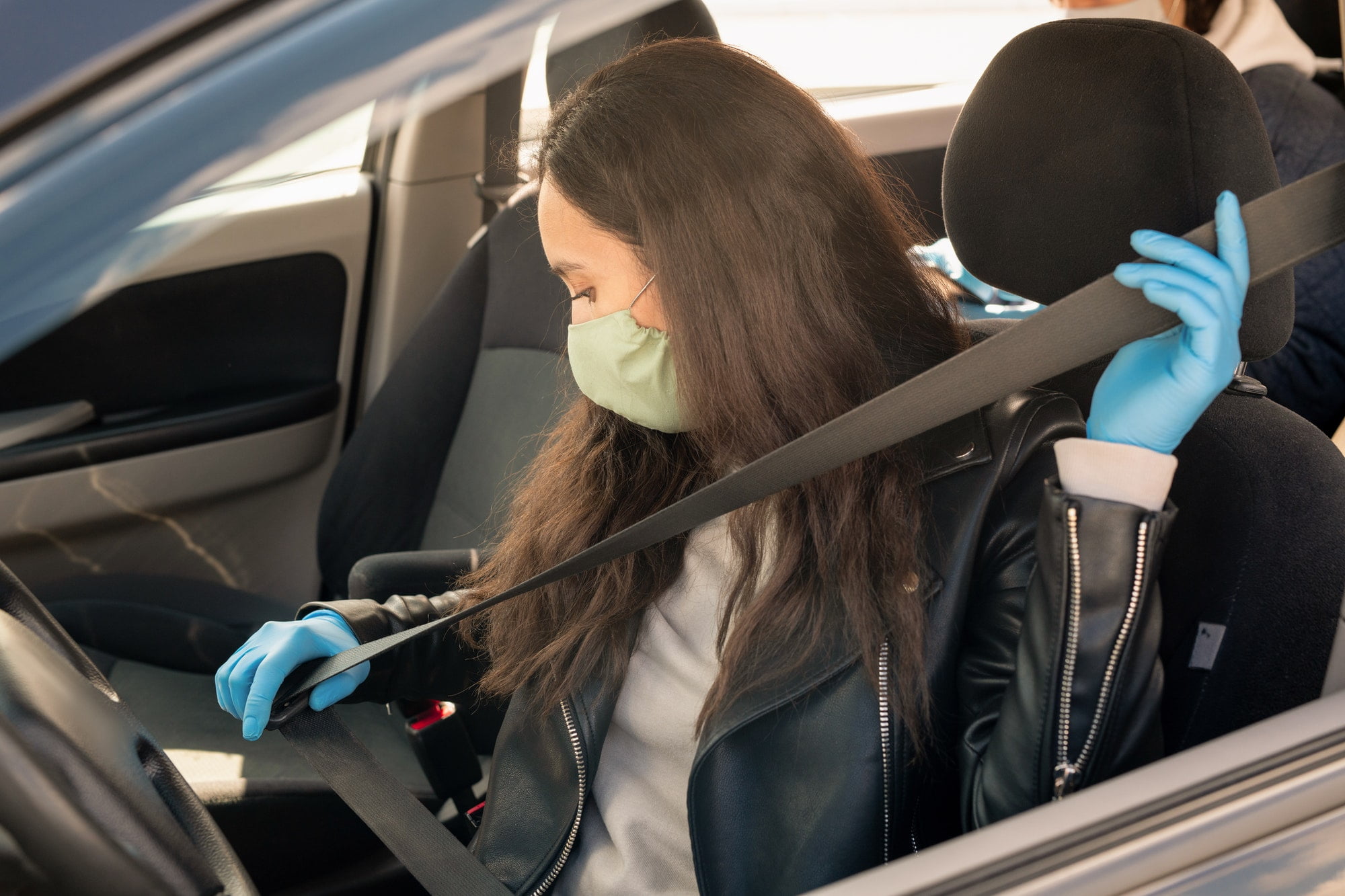 Young brunette female in leather jacket, gloves and mask fastening seatbelt
