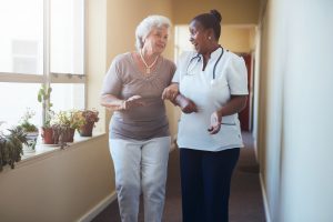 Happy healthcare worker walking and talking with senior woman