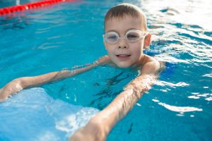 Positive little boy swimming with kickboard