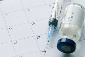 The vial with vaccine and syringe on calendar
