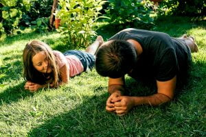 Daughter and father doing planking exercise on grass in garden. Family sport concept