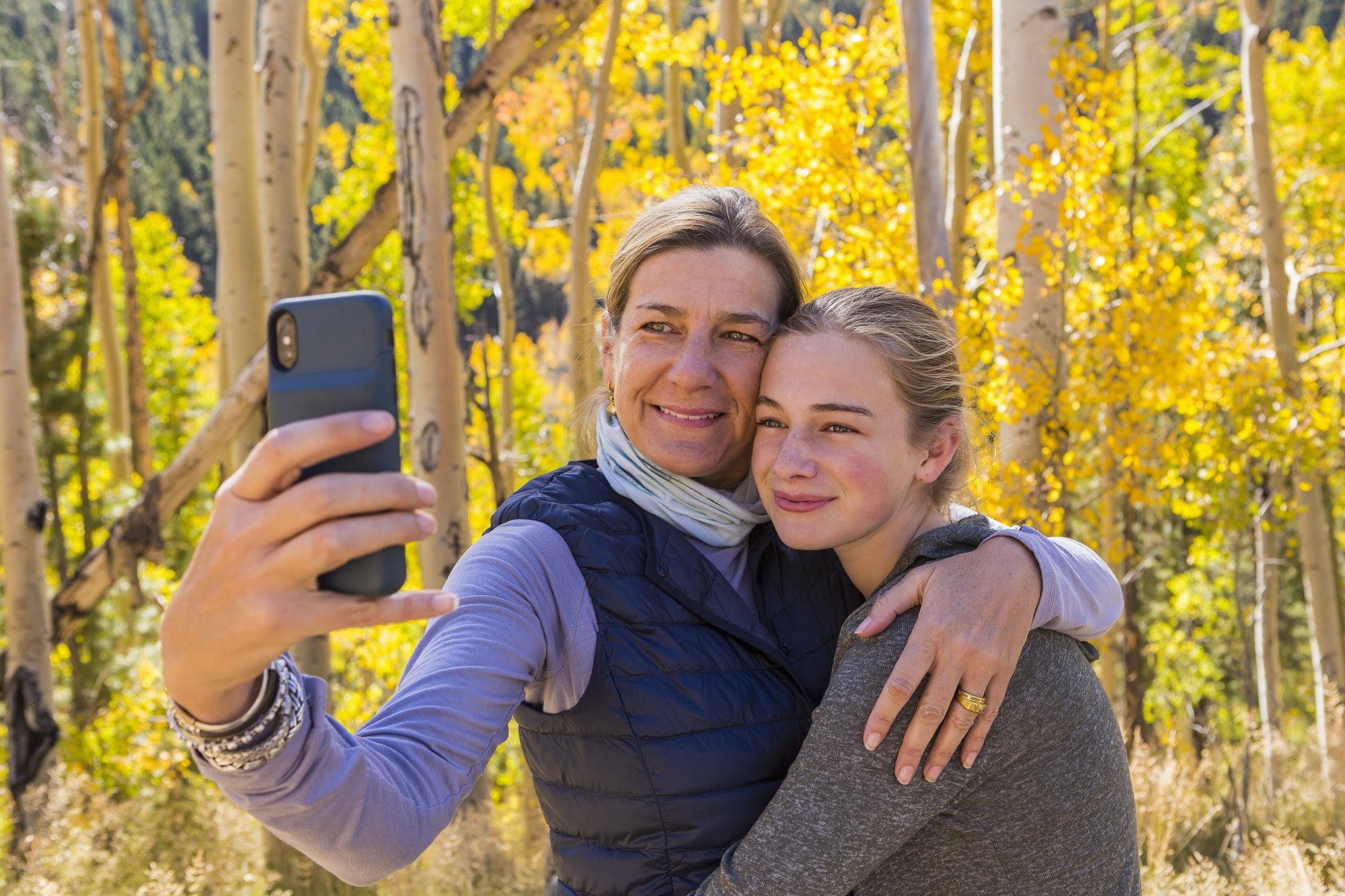 portrait of mother and her 13 year old daughter with autumn aspens in background, taking a selfie