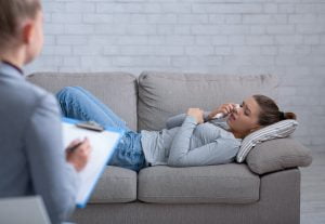 Depressed young woman consulting psychologist, lying on couch and crying
