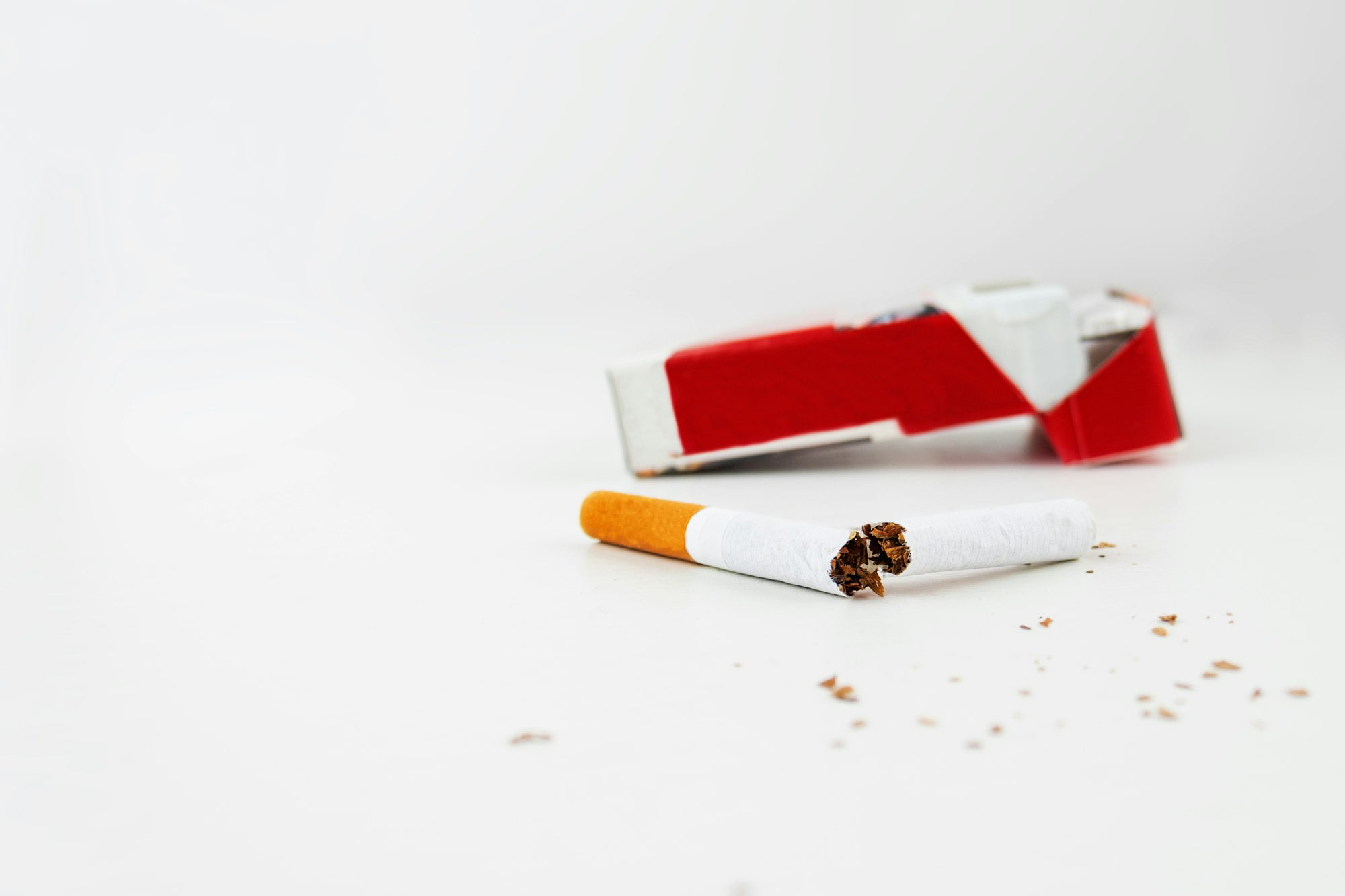 A pack of cigarettes on a white background and a broken cigarette in the foreground.