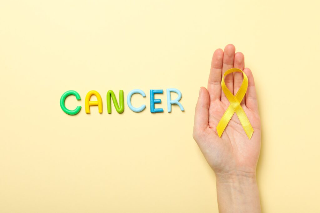 The inscription Cancer in colorful letters with a yellow ribbon